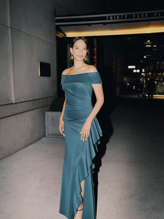 Woman in a teal off-shoulder dress standing outside at night.