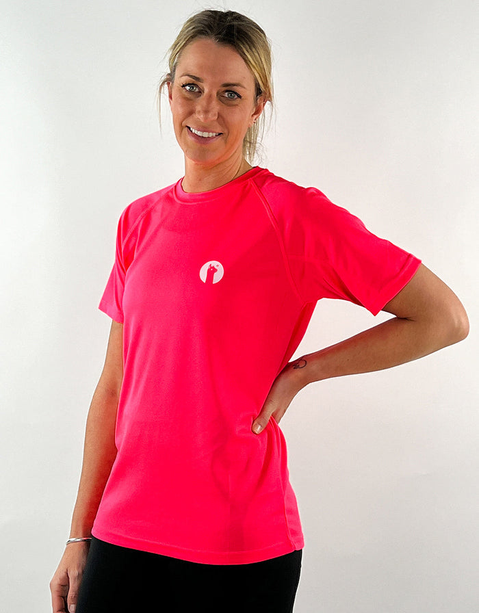 Woman wearing electric pink active t-shirt with small llama logo, standing against white background