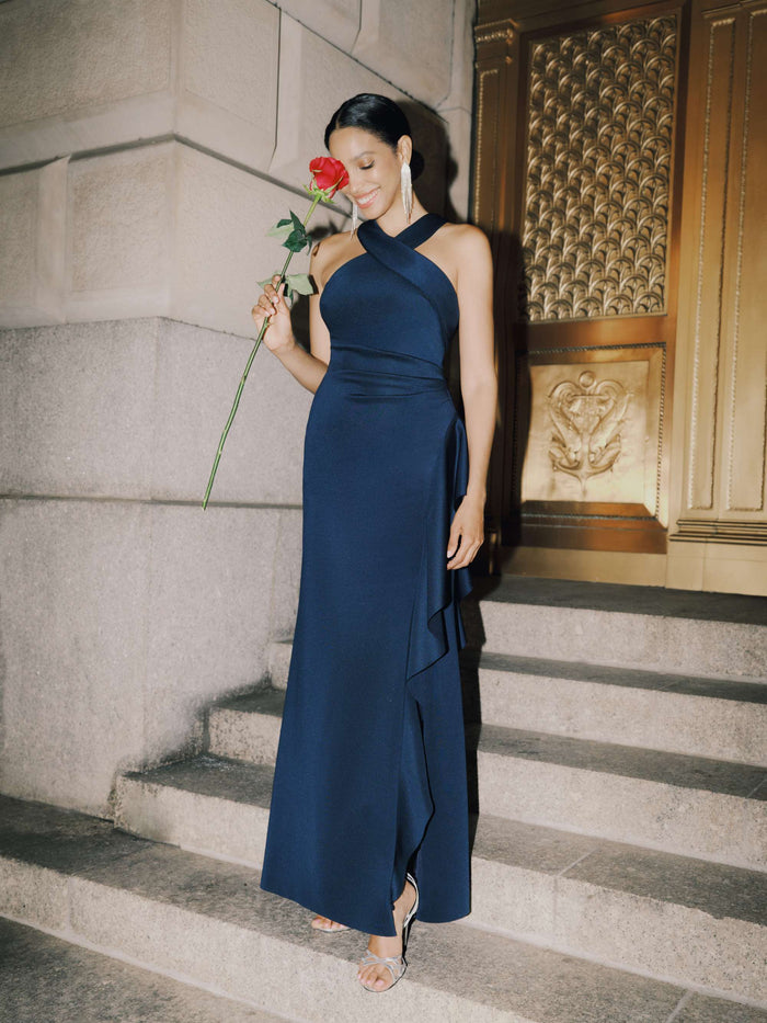 Woman in a navy blue dress holding a red rose on stone steps.