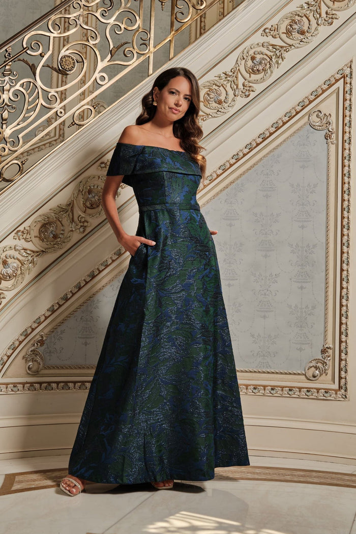 Woman in a dark blue off-shoulder dress standing in an ornate interior setting.