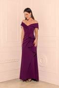 Woman wearing a purple off-shoulder evening gown against a white wall.