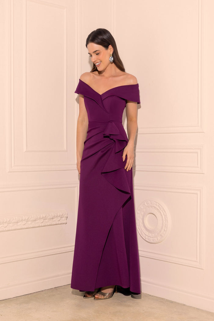 Woman wearing a purple off-shoulder evening gown against a white wall.