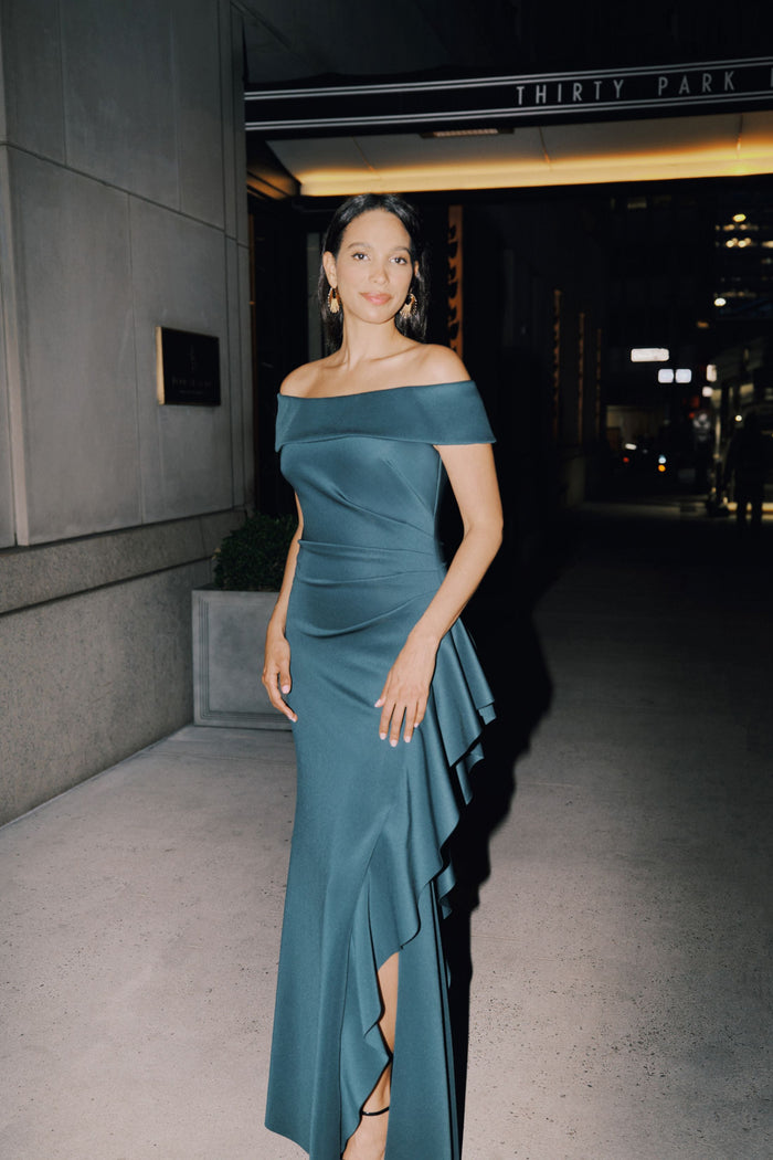 Woman in a teal off-shoulder dress standing outside a building at night.