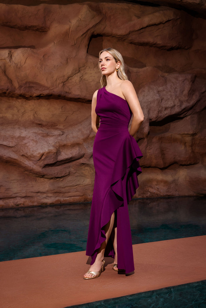Woman in a purple dress standing against a rocky background