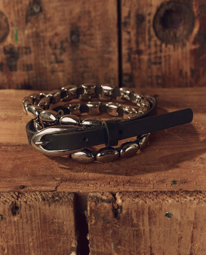 The Beaded Belt in Black With Silver by THE GREAT. F26 STETSON is coiled atop a rustic wooden surface against a knotty wood background, offering a versatile and timeless option for anyone seeking classic Western accessories.