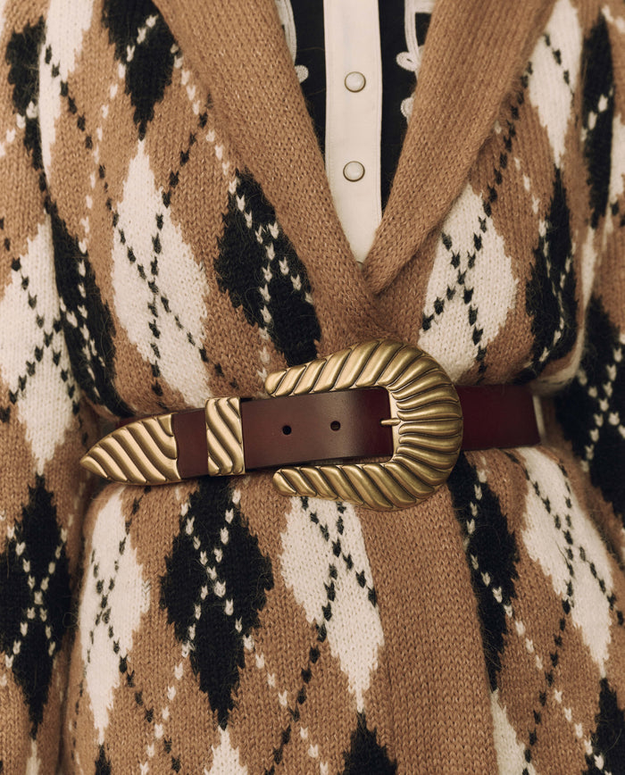 Close-up of a brown and cream argyle knit cardigan, fastened with THE GREAT. F26 STETSON & THE GREAT. The Big Buckle Belt in Cognac With Brass, featuring an oversized brass buckle and crafted from top-grain leather.