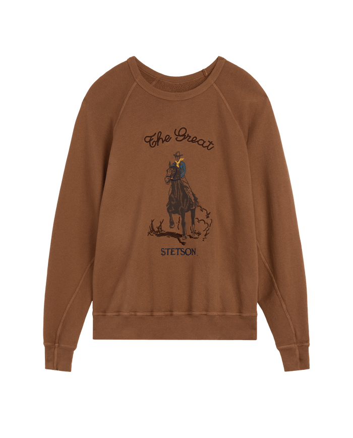 The College Sweatshirt w/ Stetson Graphic in Tobacco by THE GREAT. F26 STETSON features a vintage-style illustration of a person riding a horse and is adorned with “THE GREAT.” and “STETSON” on the front—a stylish collaboration piece.