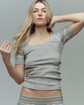 A woman with long blonde hair models THE GREAT. SU25 BABY RIB The Baby Rib Ballet Tee in Heather Grey, paired with matching pants, against a plain background.