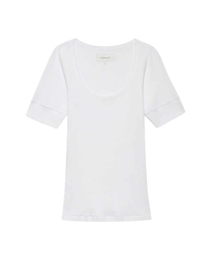 The GREAT. SU25 BABY RIB Ballet Tee in True White, a short-sleeve baby rib t-shirt with a scoop neckline, is shown laid flat on a solid black background.