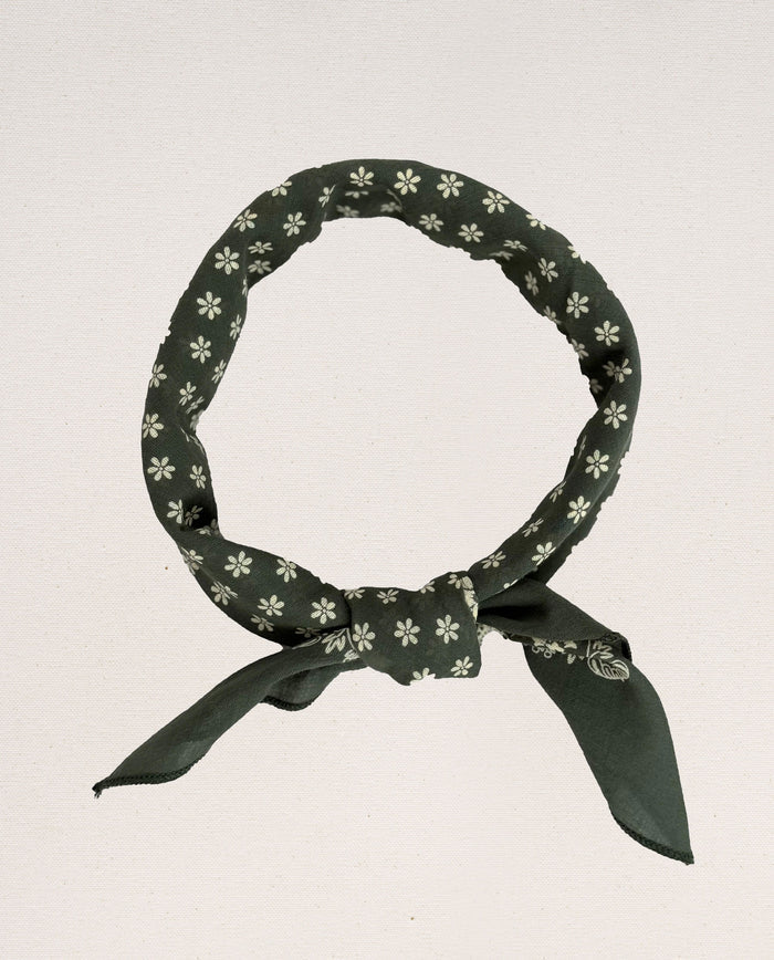 The Bandana -- Small -- Army Green by THE GREAT. SP24 D2 features a white floral pattern and is tied into a circular shape with a knot at the bottom, evoking vintage handkerchief aesthetics. Made from 100% cotton, it offers an ultra-soft feel.