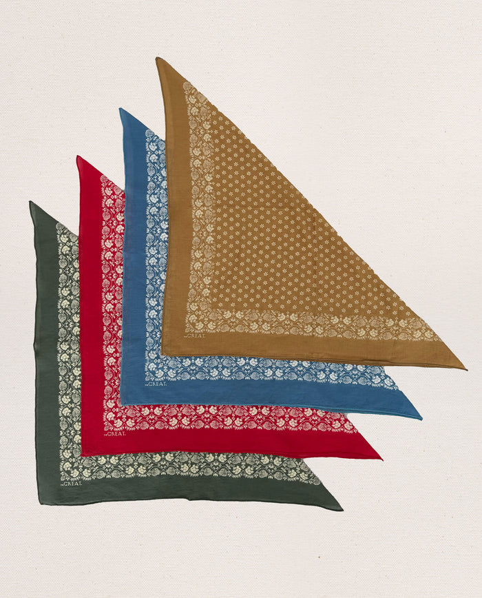 Five THE GREAT. SP24 D2 Bandanas in different colors (green, red, blue, mustard, and brown) arranged in a fan shape. Each ultra-soft handkerchief features a detailed border pattern and is made from 100% cotton for that vintage touch.