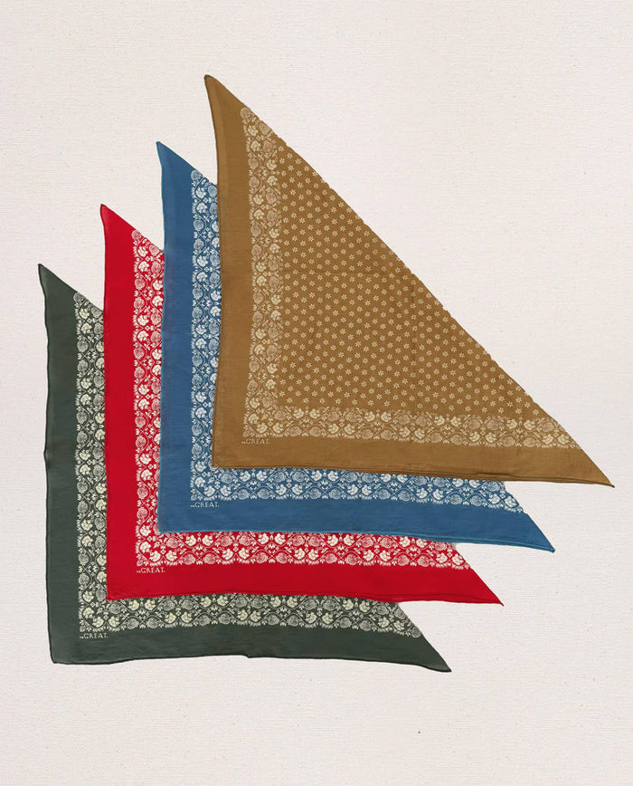 Four bright red, patterned "The Bandana. -- Small" by THE GREAT. CARRYOVER is displayed on a neutral background, folded neatly in half diagonally. Crafted from ultra-soft cotton, this vintage-inspired bandana combines comfort and style while remaining easily washable for everyday use.