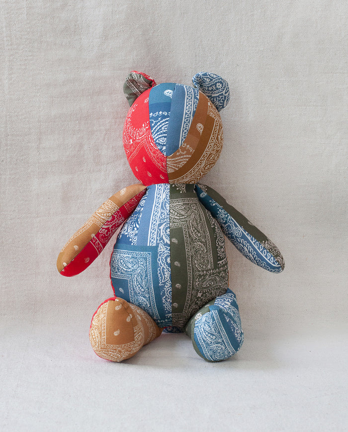 The Bear. -- Multi by THE GREAT. is an upright patchwork cotton bear crafted from red, blue, green, and tan bandana fabric, set against a light background for a vintage Western-inspired heirloom look.
