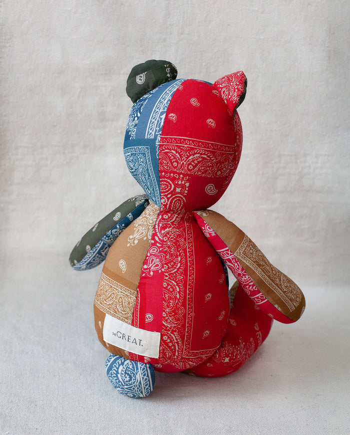 The Bear. -- Multi by THE GREAT. is a vintage Western-style patchwork cotton bear in red, blue, green, and tan bandana fabric with a small "GREAT." tag—an heirloom toy that adds charm to any collection.