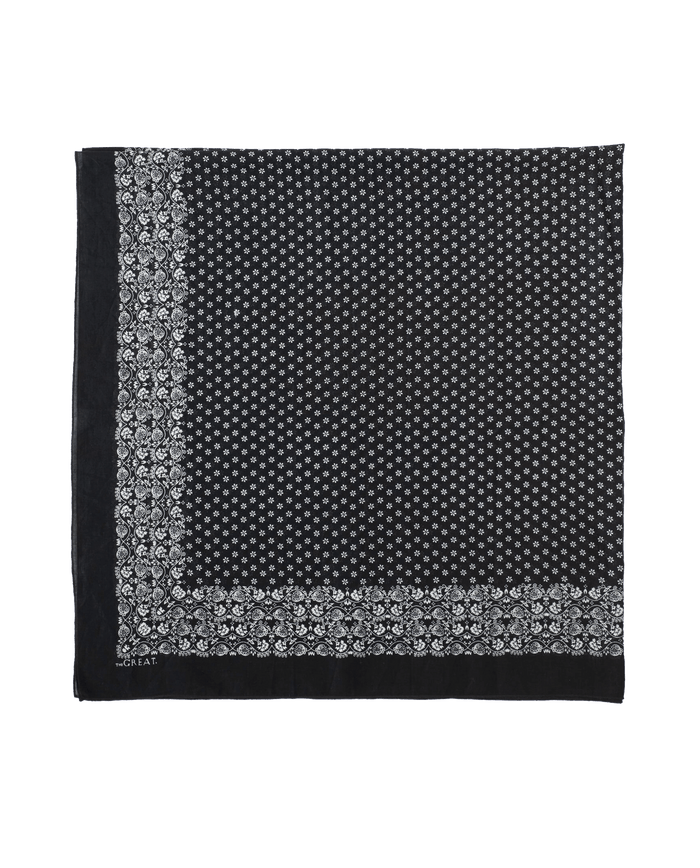 The Big Bandana in Almost Black by THE GREAT. CARRYOVER features a vintage-inspired design with a white floral border and small white center motifs, reminiscent of a classic black square handkerchief.
