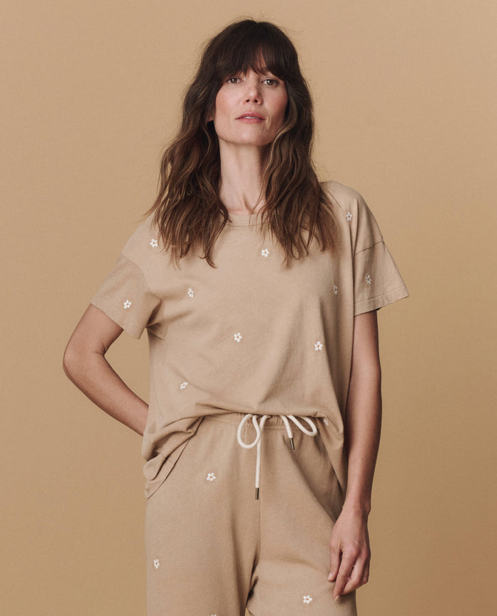 Woman wears THE GREAT. PF25 EMB KNITS The Boxy Crew. Embroidered—Khaki with Daisy Embroidery and matching pants, standing against a beige background.