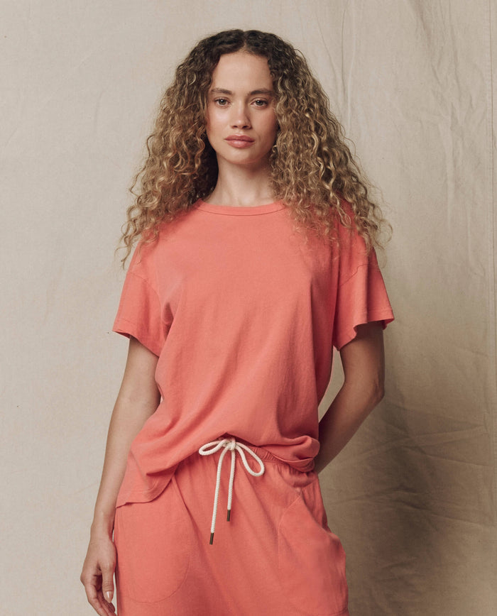 Model wearing THE GREAT. SU26 SEASONAL CORE's The Boxy Crew. Solid in Guava, styled with matching drawstring pants, in front of a plain beige backdrop.