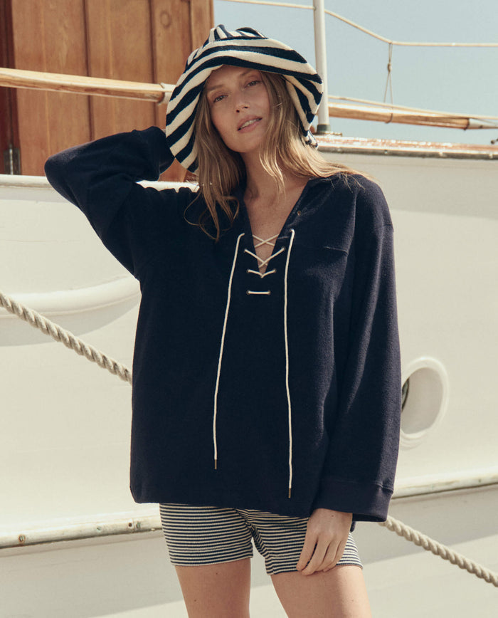 A woman stands on a boat deck in natural light, wearing THE GREAT. SU26 The Bucket Hat. -- Navy Shoreside Stripe.