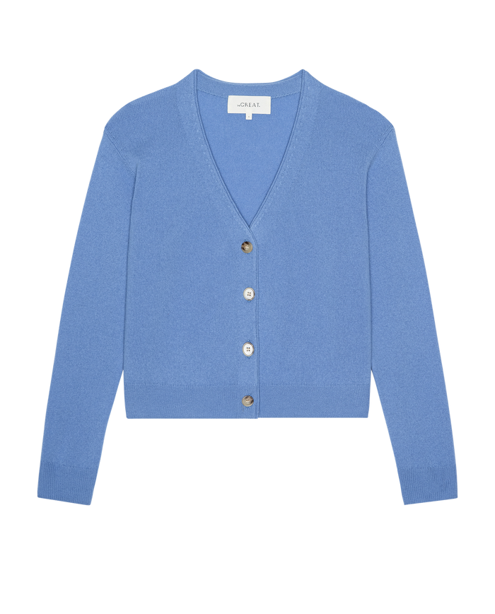 The Cashmere Tiny V Neck Cardigan by THE GREAT. PS26 in Soft Blue features long sleeves, a V-neck, and four front buttons, shown on a white background.