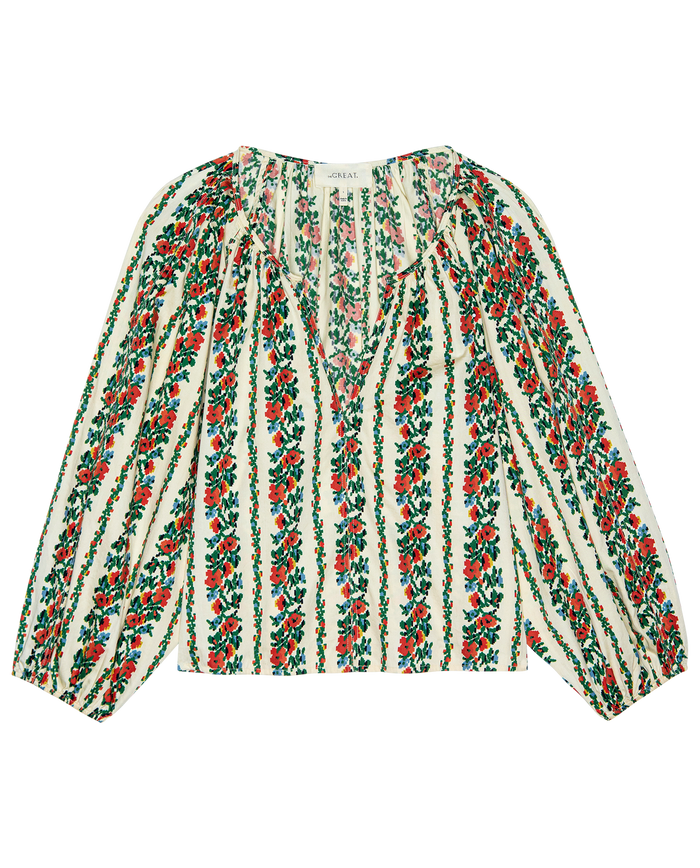 The Chariot Top by THE GREAT. PS26 is a long-sleeve blouse with an open neckline and gathered shoulders, showcasing a tapestry floral red and green pattern on white.