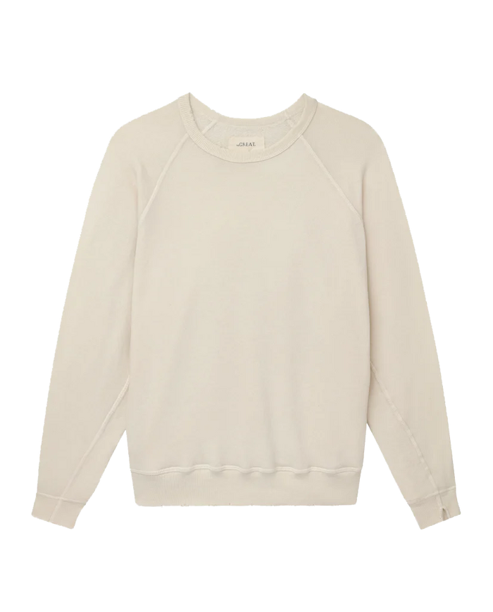 The College Sweatshirt in Washed White by THE GREAT. CORE KNITS offers the softest hand feel for ultimate comfort, featuring a plain design with a light beige shade, oversized fit, long sleeves, and ribbed cuffs and hem.