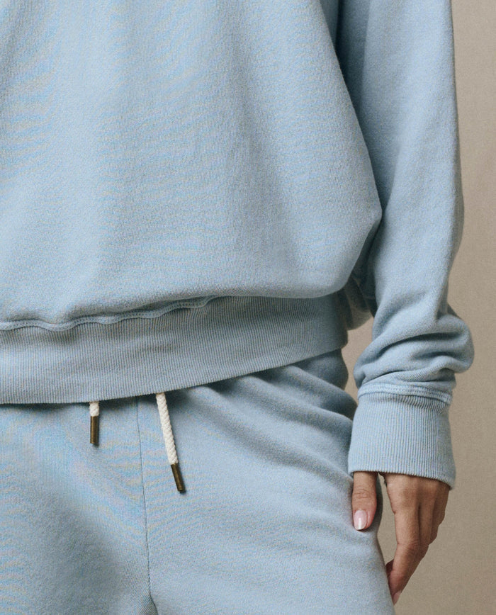 Model is wearing The College Sweatshirt in Whisper Blue by THE GREAT. SP26 SEASONAL CORE, shown from shoulders to mid-thigh, paired with matching sweatpants featuring white drawstrings and a hand resting by their side.