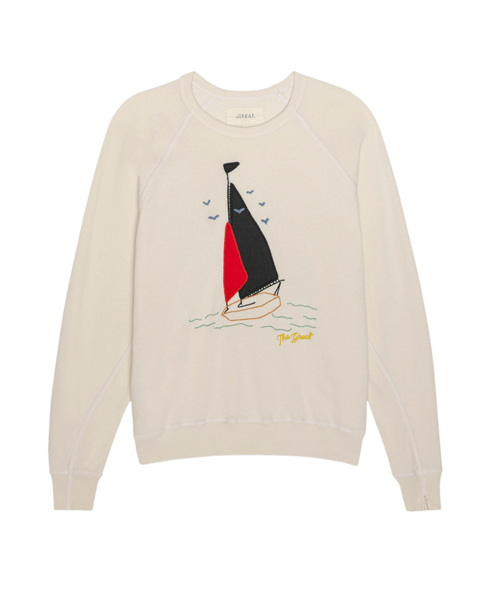 The College Sweatshirt W/ Sailing Boat Applique by THE GREAT. SU26 in washed white features a sailing boat applique with black and red embroidered sails, small waves, flying birds, and "The Great" in yellow script.
