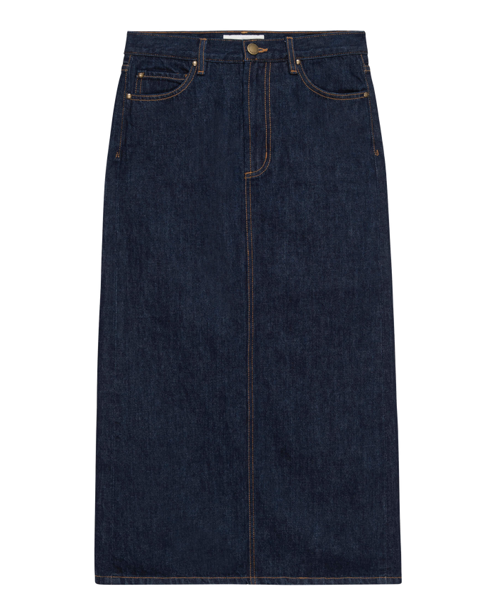 The Column Skirt in Midnight Rinse by THE GREAT. PF24 showcases a timeless column silhouette in dark denim, enhanced with a front button and zipper, two front pockets, and contrast stitching for a touch of modern flair.