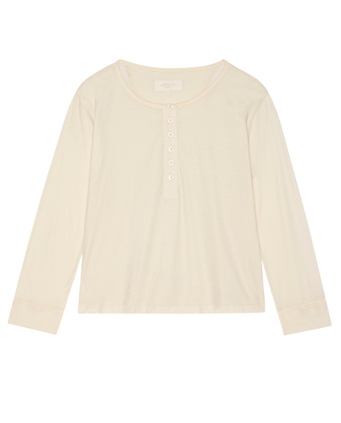 The Crop Sleep Henley in Washed White by THE GREAT. H25 SLEEP is a cozy, long-sleeve jersey shirt crafted from 100% cotton with a round neck and five-button placket, shown laid flat on a white background.