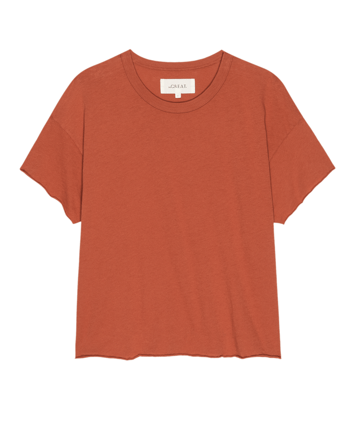 The Crop Tee. Solid -- Desert Clay by THE GREAT. SU25 SEASONAL KNITS is a rust-colored, short-sleeve crop top with a crew neckline, perfect for casual women's fashion, shown against a white background.