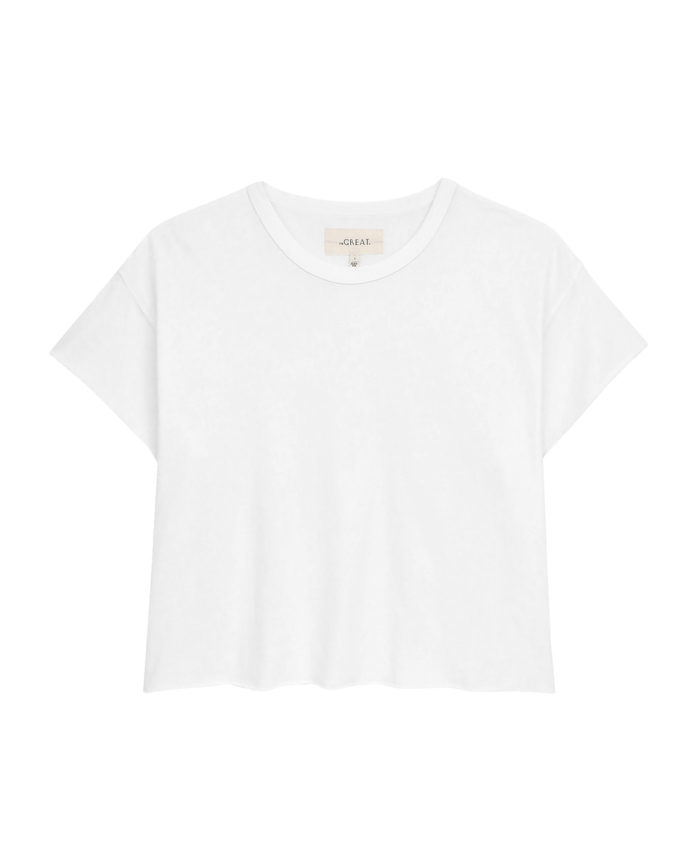 The Crop Tee in True White by THE GREAT. CORE KNITS features a plain white cotton design with short sleeves and a round neckline, set against a black background.