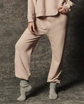 Wearing THE GREAT. PF26 DANCER KNIT BODIES' The Dance Pant in Ballet Pink, a person pairs the look with a matching sweatshirt and gray socks, standing on a textured surface with one foot flat and the other tiptoe—an effortless showcase of relaxed, comfortable dancewear style.
