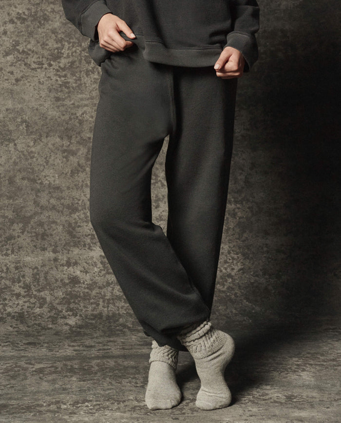 Wearing THE GREAT.'s The Dance Pant in Flat Charcoal (PF26 DANCER KNIT BODIES), this person stands on a textured surface with ankles crossed, paired with a matching top and light gray socks.
