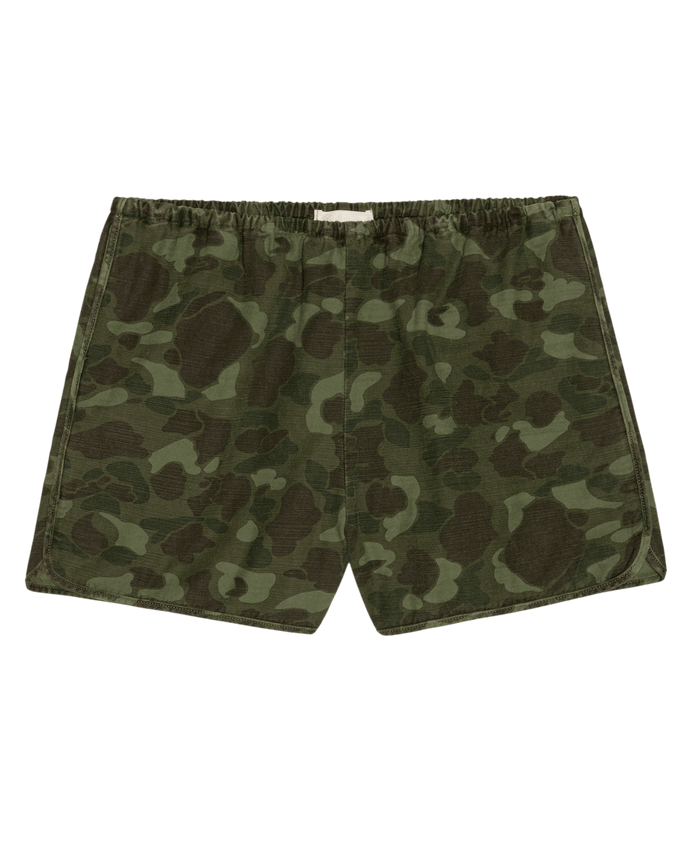 THE GREAT. SU26 The Dolphin Short. -- Desert Camo features green camouflage-patterned dolphin shorts with an elastic waistband, shown flat on a white background.