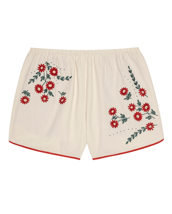 The Dolphin Short in natural by THE GREAT. SU26 features red field floral embroidery with green leaves, an elastic waistband, and red trim along the hem.