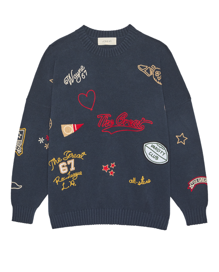 The GREAT. SP26 D1 Embroidered Oversize Crew Pullover in True Navy features assorted red, yellow, and white patches—including stars, text, badges, and vibrant designs—offering a playful twist to your wardrobe.