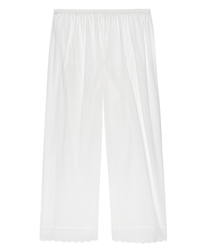 The Eyelet Easy Sleep Pant in True White by THE GREAT. PS25 SLEEP is a pair of white, wide-legged pants crafted from cotton voile fabric with an elastic waistband and scalloped hems adorned with delicate eyelet lace trim.