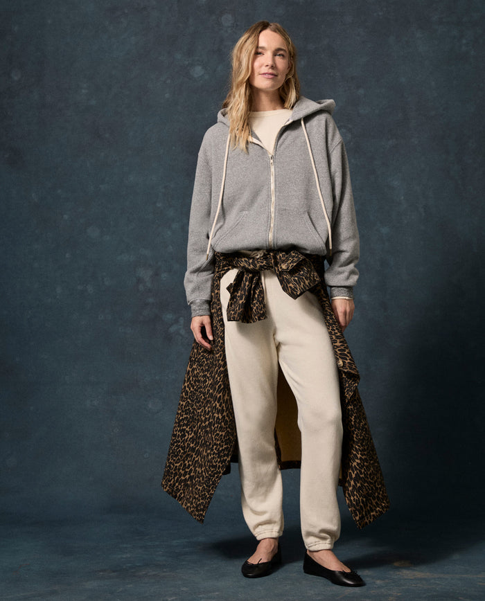 A person stands against a dark backdrop, wearing THE GREAT.’s The Fleece Campus Hoodie in Dark Heather Grey.