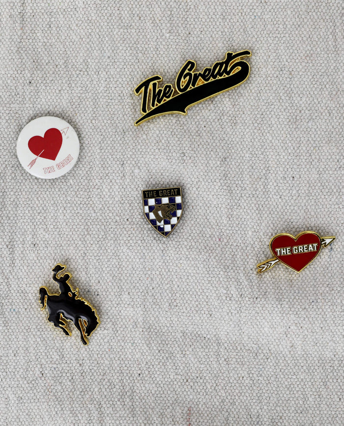 Introducing The Great Five Pack Enamel Pins by THE GREAT. HOL 22 ACCESSORIES: a set of five collegiate-inspired enamel pins on fabric. This multi pack includes two pins with "The Great" in script, a heart pin labeled "The Great," a badge pin, and a leaping mustang figure. Featuring bold colors, these pins are perfect for customizing your look.