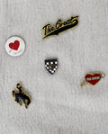 Introducing The Great Five Pack Enamel Pins by THE GREAT. HOL 22 ACCESSORIES: a set of five collegiate-inspired enamel pins on fabric. This multi pack includes two pins with "The Great" in script, a heart pin labeled "The Great," a badge pin, and a leaping mustang figure. Featuring bold colors, these pins are perfect for customizing your look.