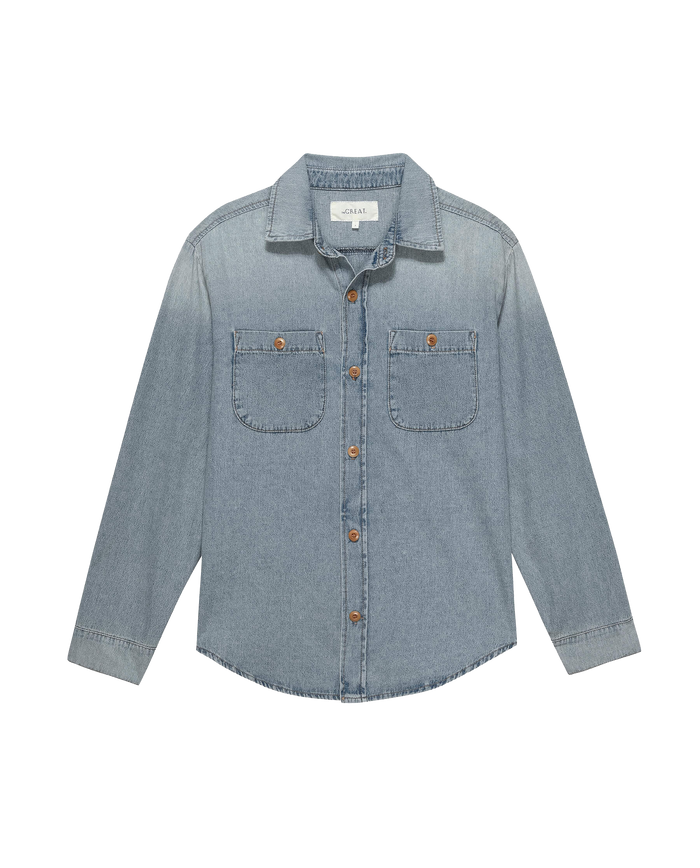 The Harbor Shirt in Asphalt Wash by THE GREAT. FALL 23 AUGUST CAP is a vintage-inspired piece, crafted from light blue denim and designed with long sleeves, a classic collar, button closures, and two front pockets.