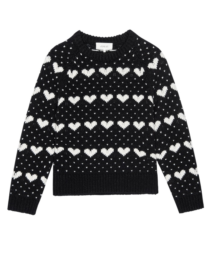 The Heart Crew.--Black With Pearl by THE GREAT. PS26 is a vintage-style wool crewneck sweater with rows of white heart and dot patterns, shown on a plain white background.