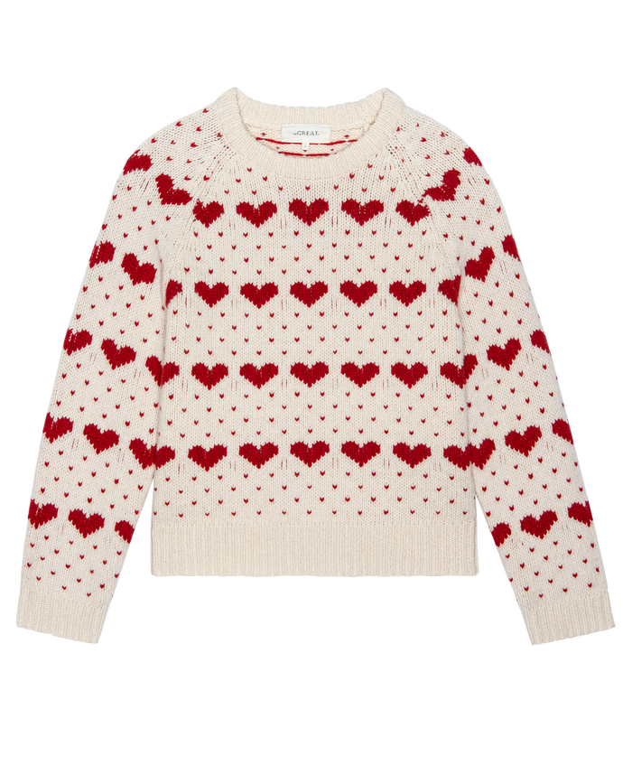 The Heart Crew. -- Pearl with Red by THE GREAT. PS26 is a vintage-inspired sweater featuring rows of red heart motifs across the front, sleeves, and neckline on a cream base.