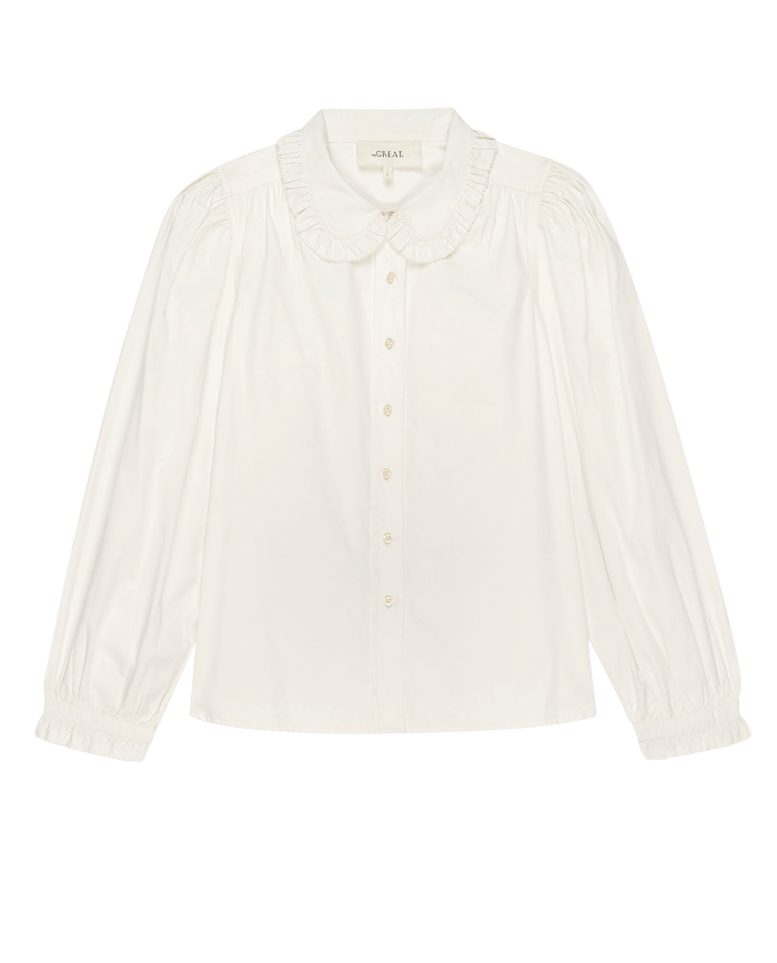 The Hemingway Top by THE GREAT. PS25 is a women's fashion blouse in white, featuring a soft ruffled collar, button-down front, and long sleeves with gathered cuffs.