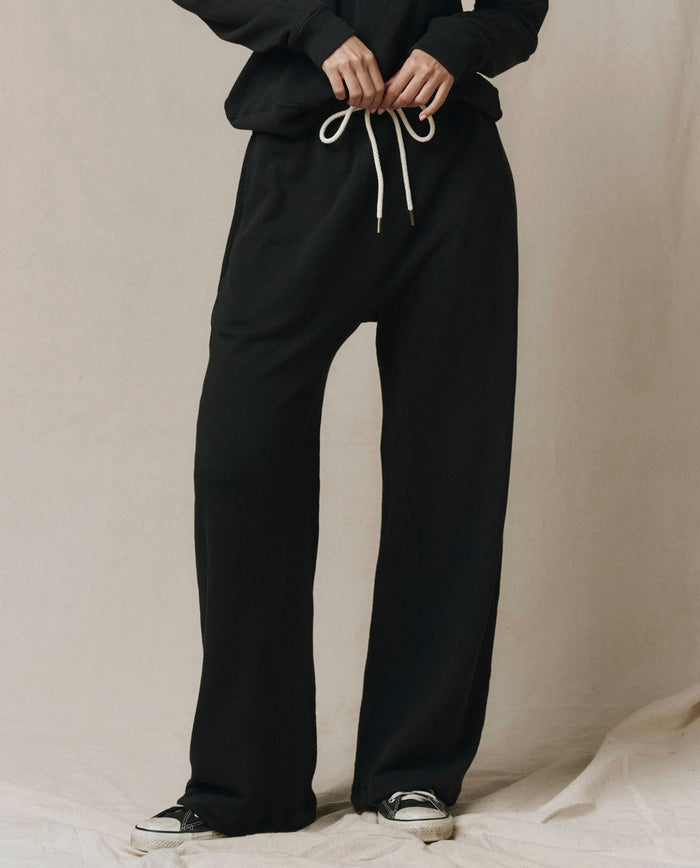A person wears SP26 New Knits' The Horseshoe Sweatpant in Almost Black with white drawstrings, a matching sweatshirt, and black-and-white sneakers, standing against a neutral background for a relaxed loungewear vibe.