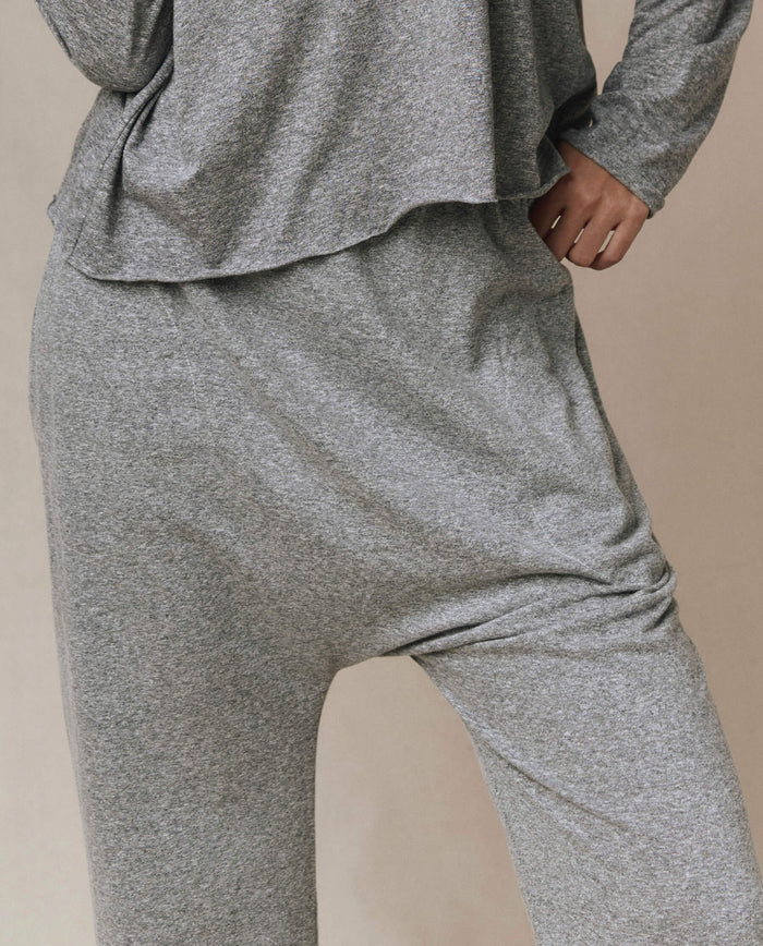 Model wears THE GREAT. CORE KNITS The Jersey Crop Pant in heather grey, featuring a loose fit, elastic waist, and straight leg; only torso, hips, and upper legs visible with left hand on hip.