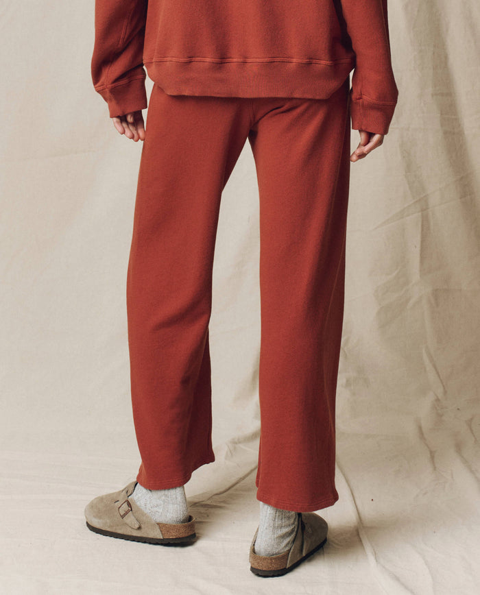 Model is wearing The Lap Sweatpant. Solid -- Brick and matching sweatshirt by THE GREAT. F25 SEASONAL KNITS, styled with gray socks and beige Birkenstock sandals, standing on a neutral fabric backdrop.