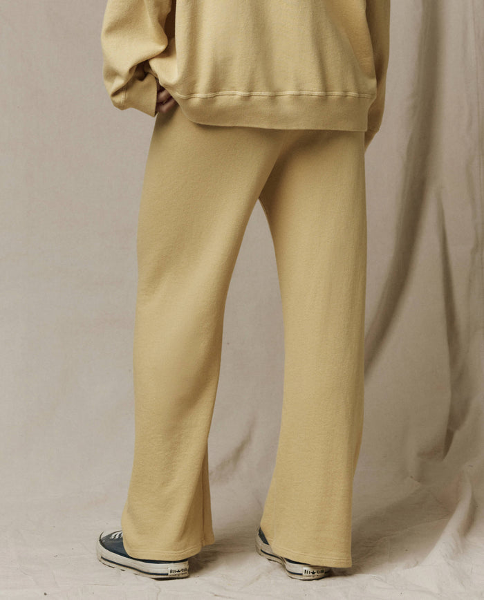 Person wearing loose-fitting Butter Yellow The Lap Sweatpant from THE GREAT. SP26 SEASONAL CORE, a matching oversized sweatshirt, and gray sneakers stands on a light fabric backdrop.