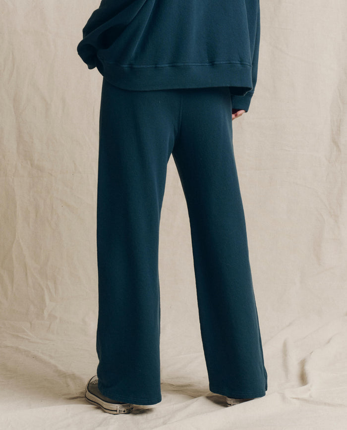 Wearing THE GREAT.’s The Lap Sweatpant in Solid -- Dark Slate from the F26 SEASONAL CORE collection, a person stands facing away on a light beige background, embodying the effortless style of handcrafted Los Angeles design.