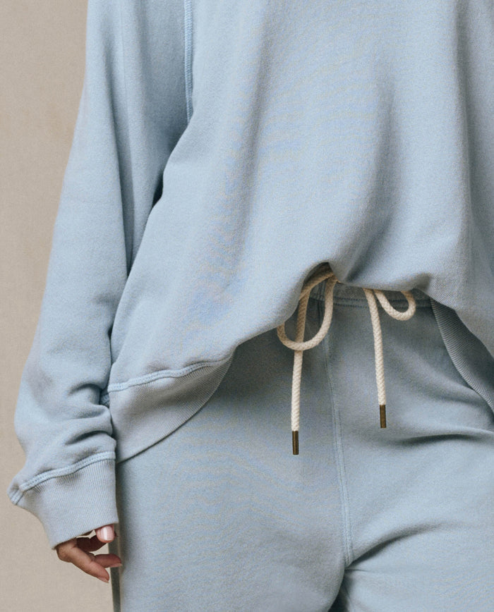 Person wearing THE GREAT. SP26 SEASONAL CORE "The Lap Sweatpant" in Whisper Blue, a loose-fitting, wide-leg sweatpant with white drawstring, shown from the shoulders down.
